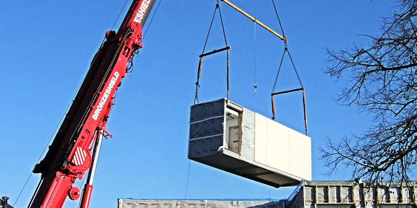 A crane lifts a prefabricated volumetric module onto a building